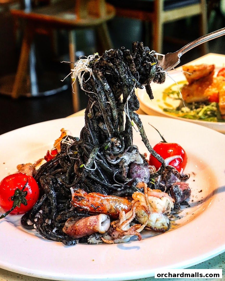 A fork lifts a portion of black squid ink pasta with seafood and cherry tomatoes.