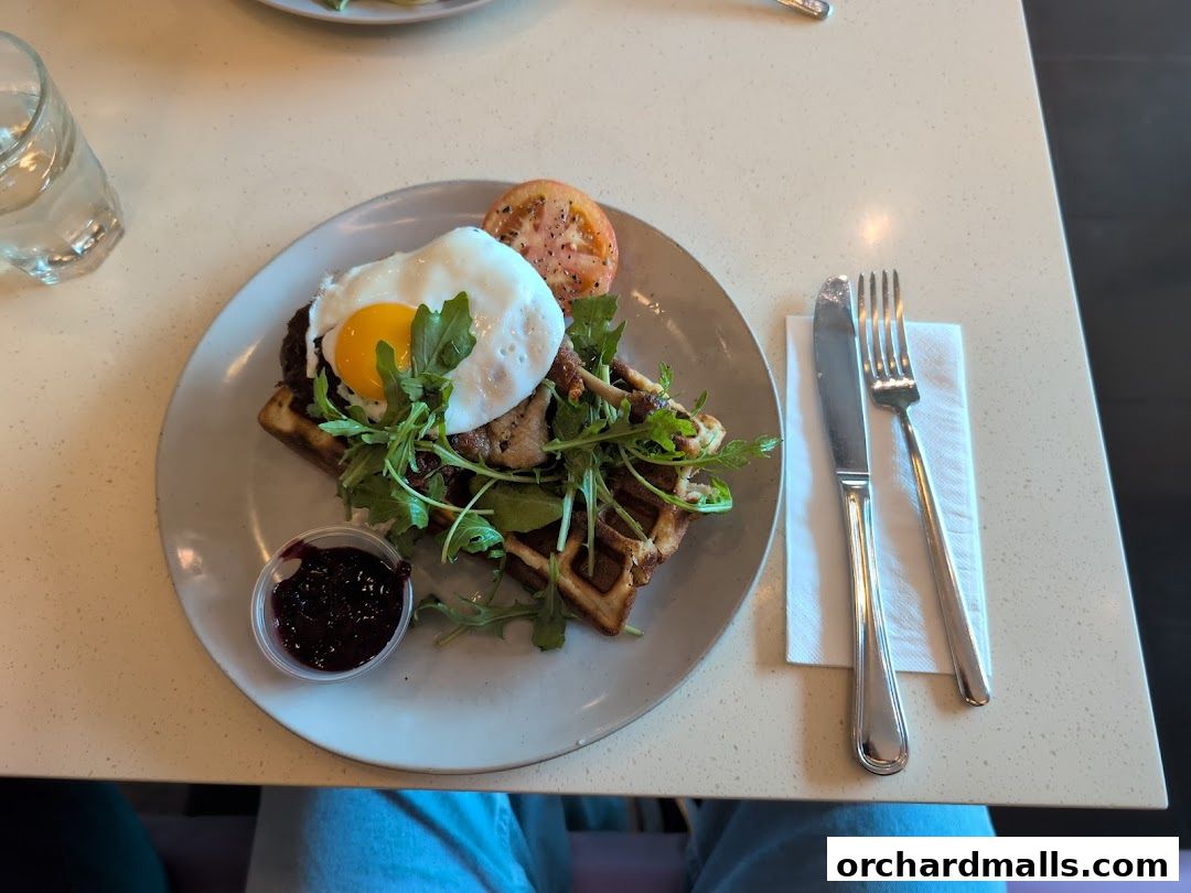 A savory waffle topped with a fried egg, greens, and meat, served with jam.