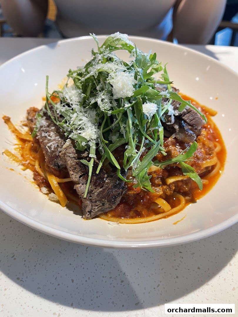 A close-up of a delicious pasta dish with sliced steak and arugula, topped with cheese.