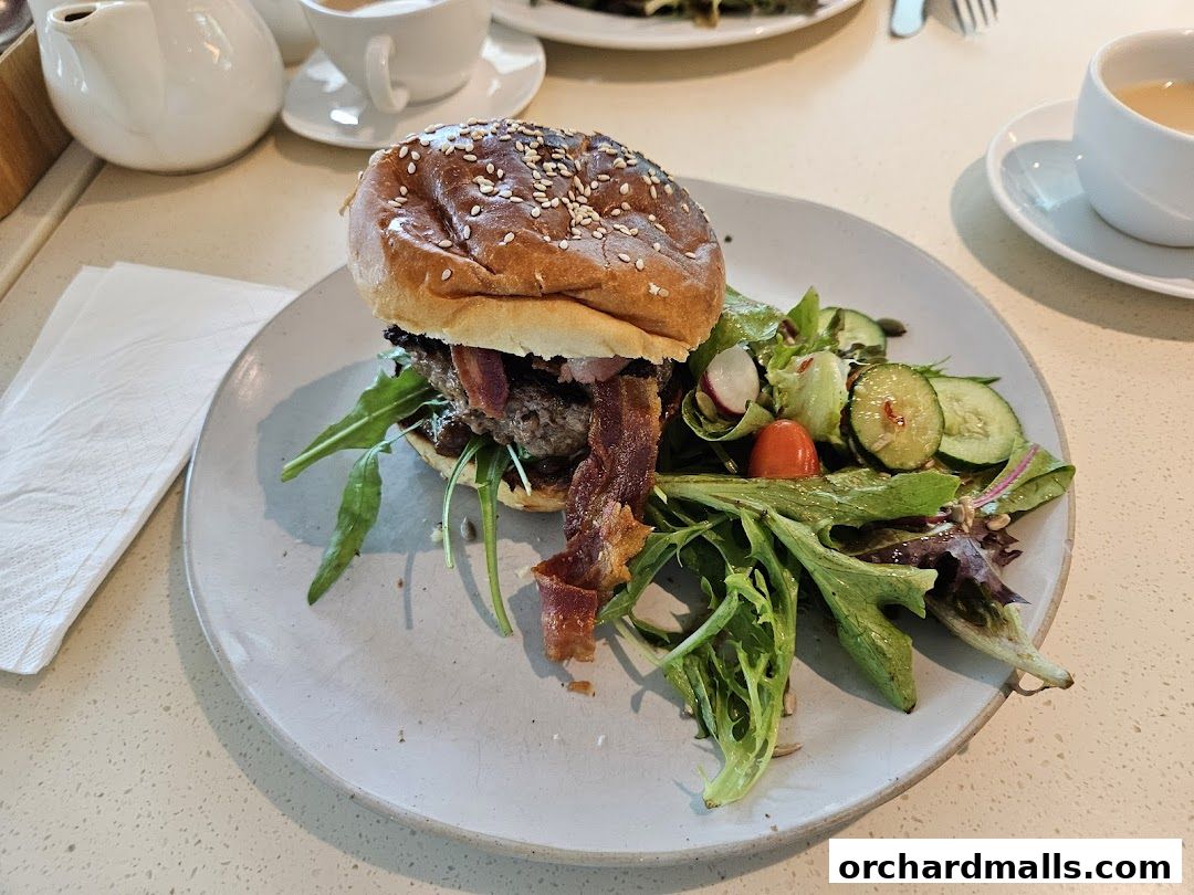 A juicy burger with bacon and a side salad served on a plate with a cup of tea.