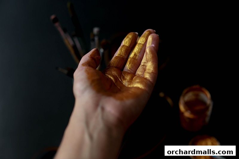 A hand covered in gold paint with brushes and paint pots in the background.