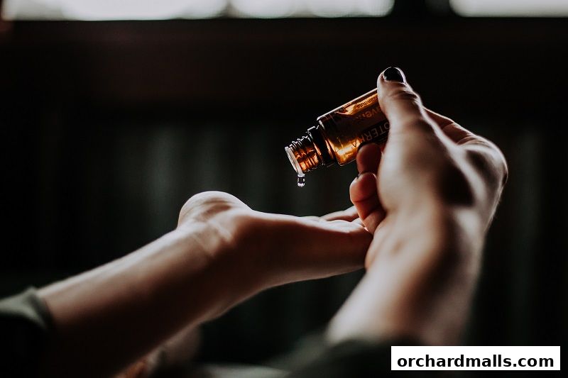 A hand holding a bottle of essential oil, dripping oil onto another hand.