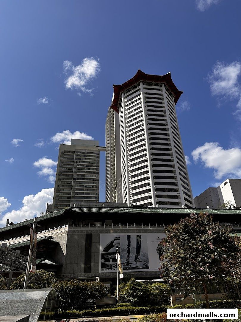 Modern skyscrapers with traditional Asian-inspired roofs under a blue sky with clouds.
