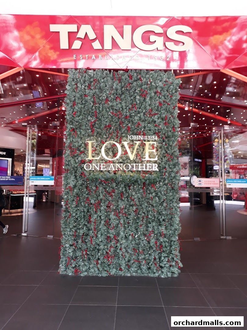 The entrance of TANGS department store decorated with a festive green wall featuring the words 'LOVE ONE ANOTHER'.