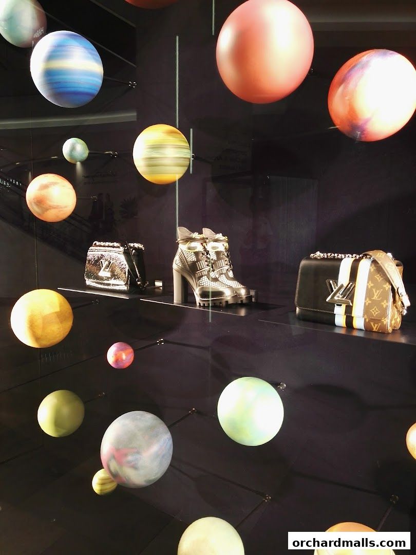 A retail display featuring luxury handbags and shoes with a celestial-themed backdrop of planets.