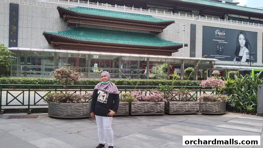 A woman stands in front of a building with traditional Asian-inspired architecture and a large advertisement.