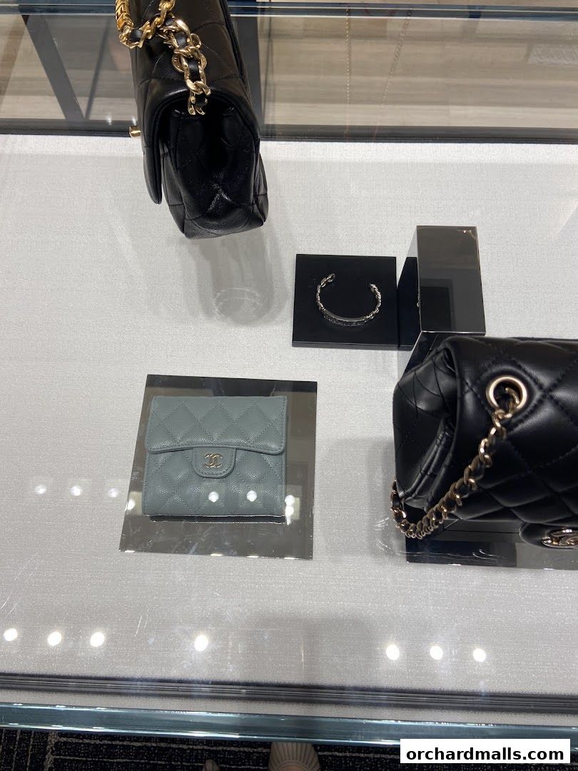 Chanel handbags and a wallet displayed on a glass surface with reflections.