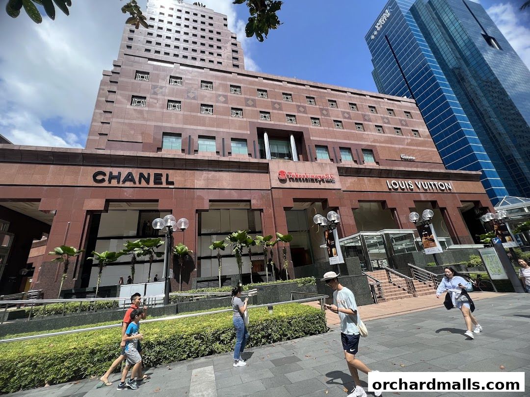 Chanel and Louis Vuitton storefronts on a modern building exterior with people walking by.