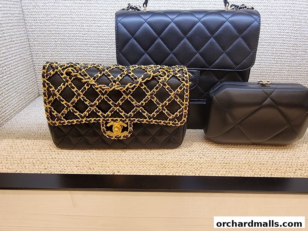 Three elegant black Chanel handbags with gold chain detailing displayed on a textured surface.