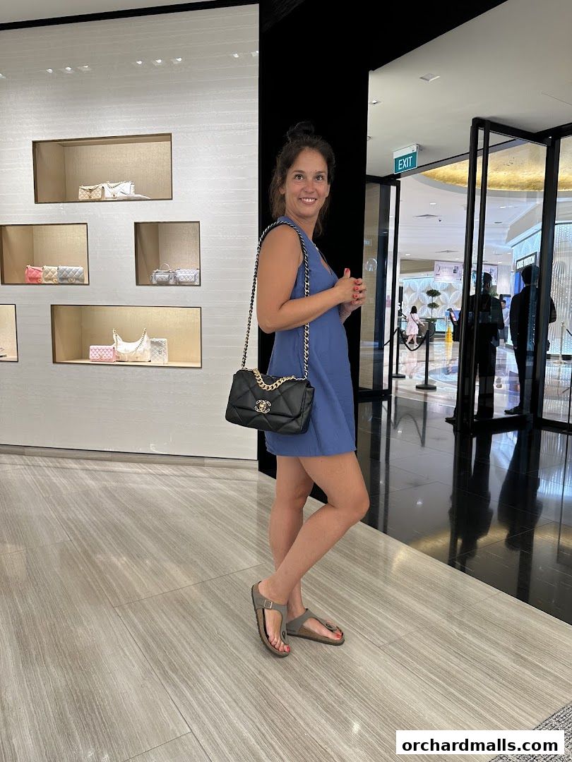 A woman smiles while holding a Chanel handbag inside a luxury boutique.