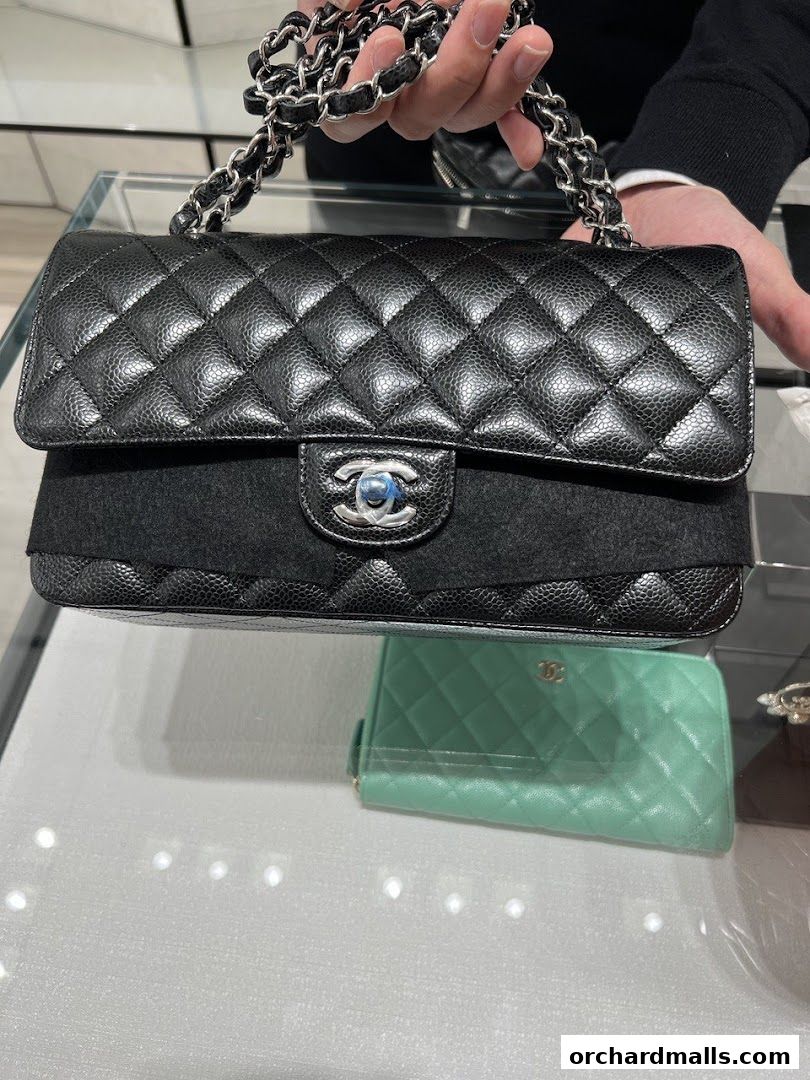 A person holds a black quilted Chanel handbag with a silver chain strap.