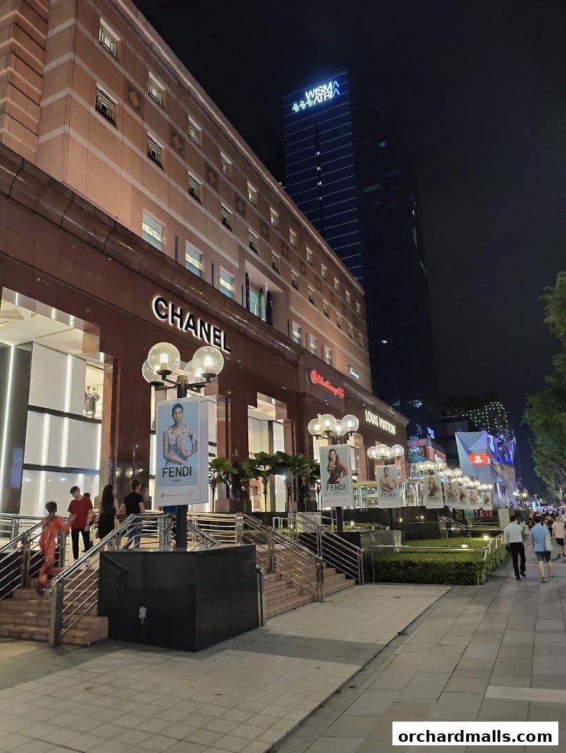 Chanel store entrance at night with illuminated signage and advertisements.