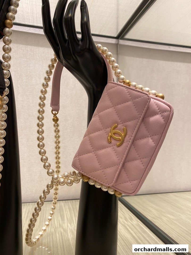 A pink Chanel handbag with pearl embellishments displayed on a black mannequin hand.
