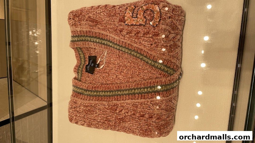A pink Chanel sweater with sequined '5' and pearl details displayed in a store window.