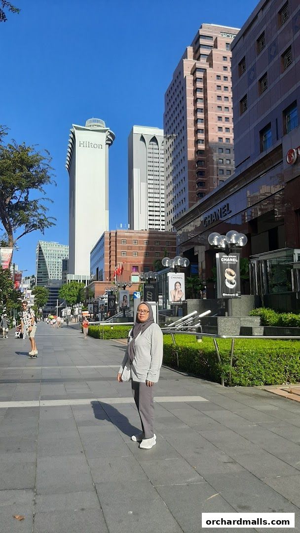 A woman stands on a paved walkway in front of the Chanel Watches and Fine Jewellery store.