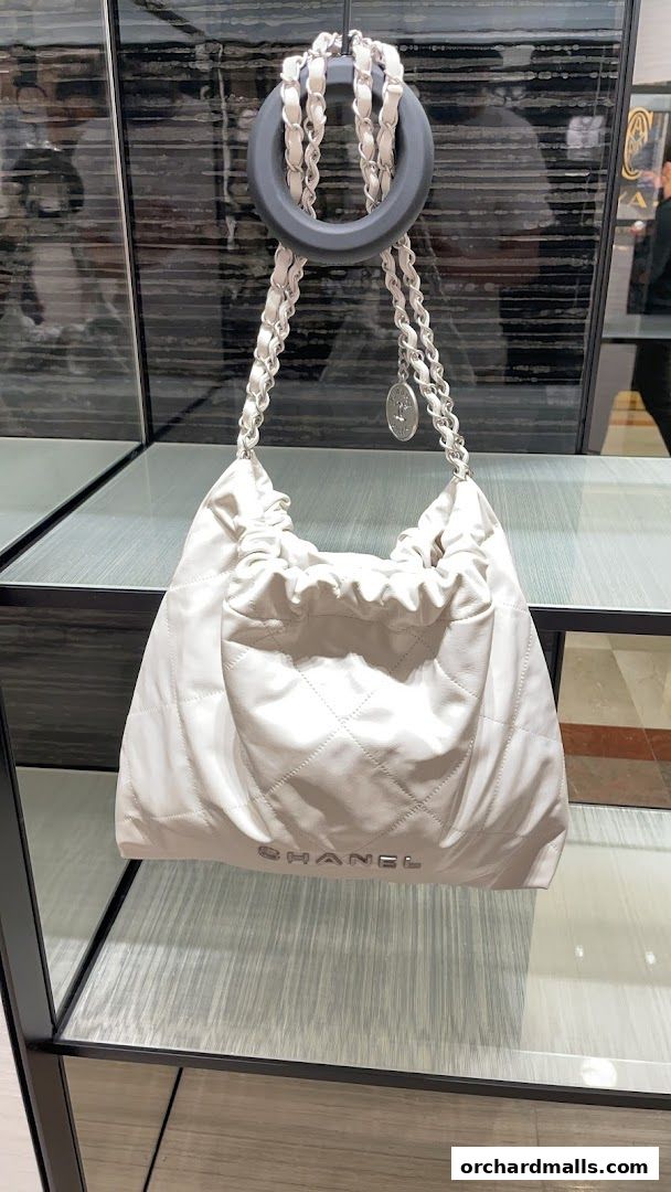 A white Chanel handbag with quilted detailing and chain straps displayed in a store.