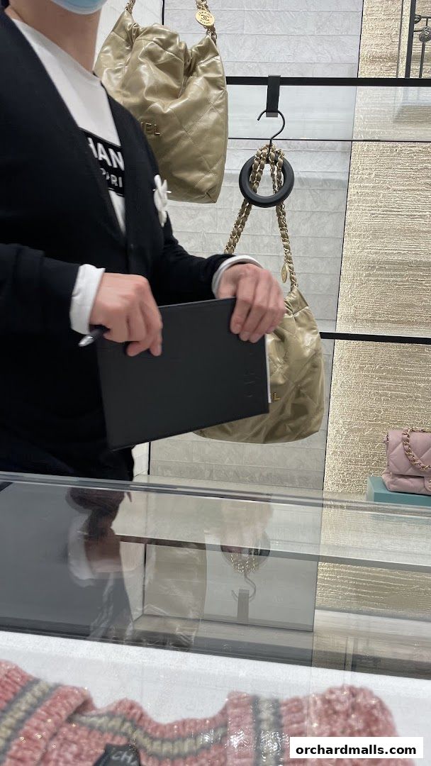A person in a Chanel store holds a black notebook near display bags and jewelry.