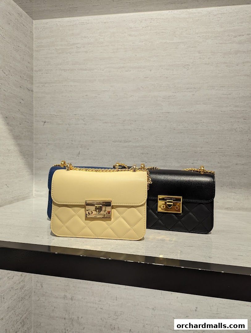 Two quilted crossbody bags, one cream and one black, displayed on a shelf.