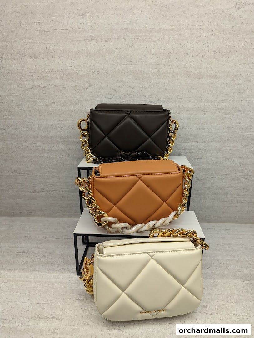Three quilted crossbody bags with chunky chain straps in brown, orange, and cream.