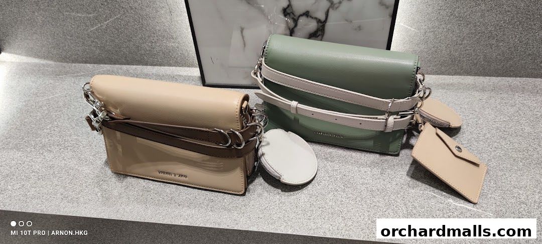 Two stylish Charles & Keith handbags, one beige and one sage green, displayed on a counter.