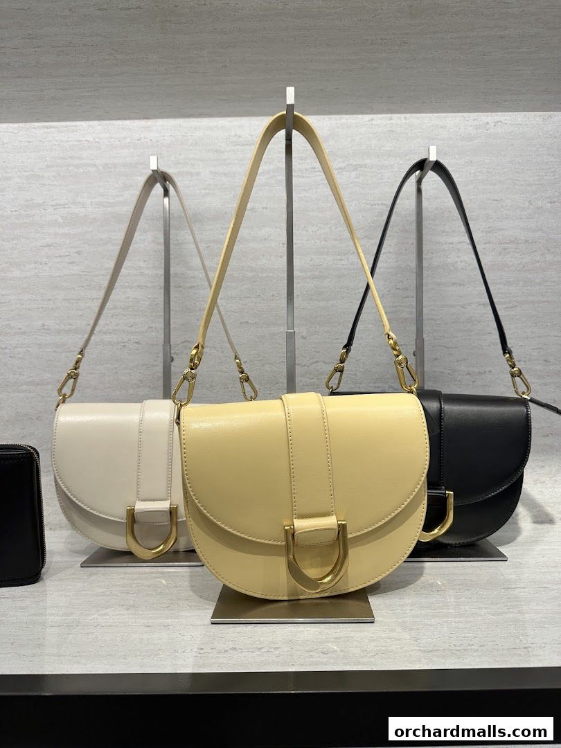 Three stylish saddle bags in cream, yellow, and black are displayed on stands.
