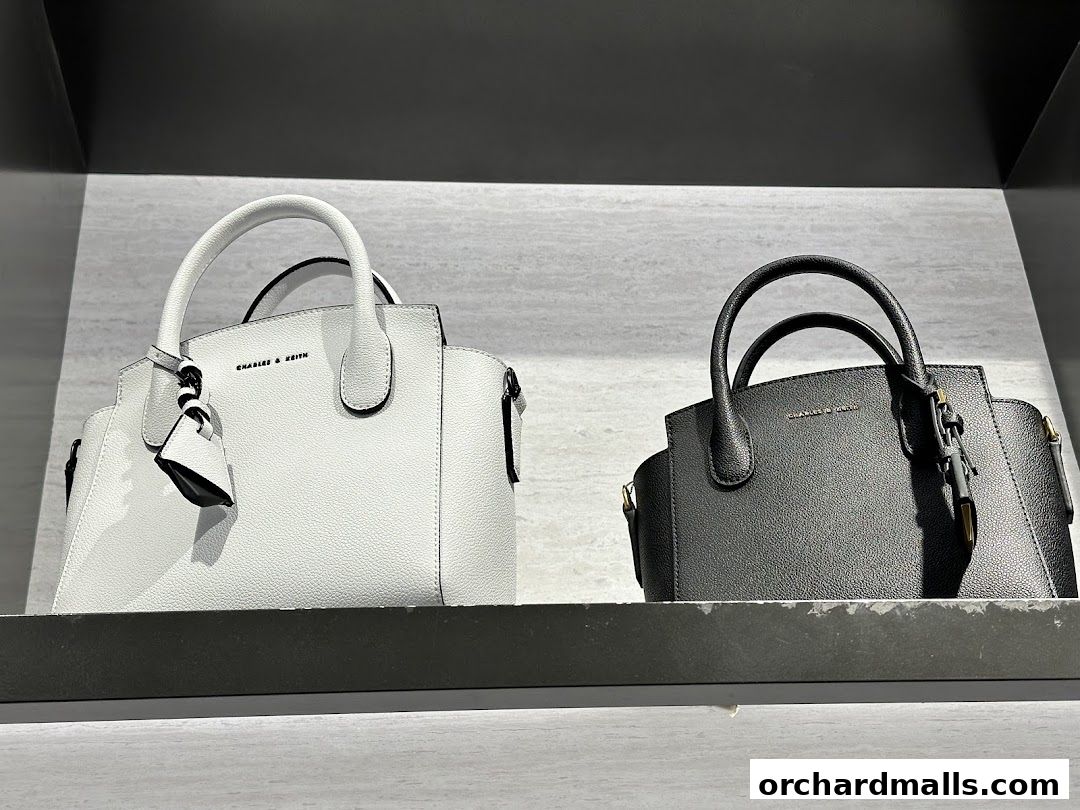 Two Charles & Keith handbags, one white and one black, displayed on a shelf.
