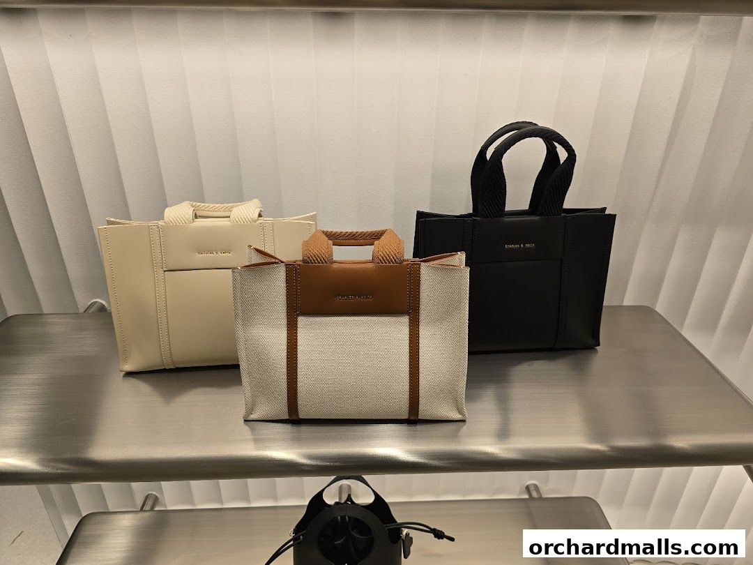 Three stylish tote bags in cream, beige, and black displayed on a metallic shelf.