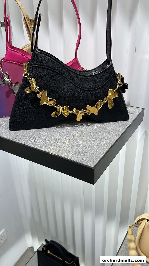 A black handbag with a unique gold chain detail is displayed on a shelf.