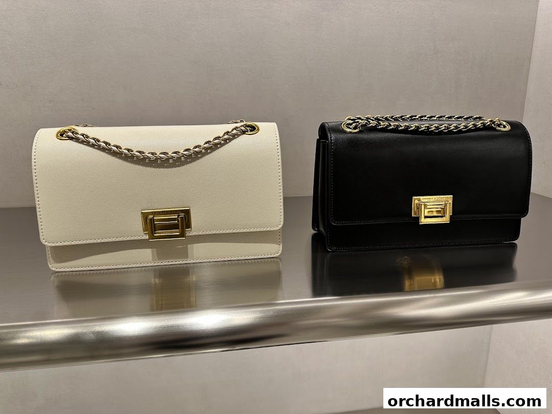 Two stylish chain-strap shoulder bags, one in cream and one in black, displayed on a shelf.