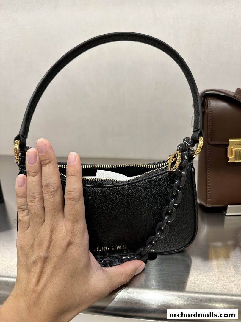 A hand is shown next to a black Charles & Keith handbag with a chain detail.