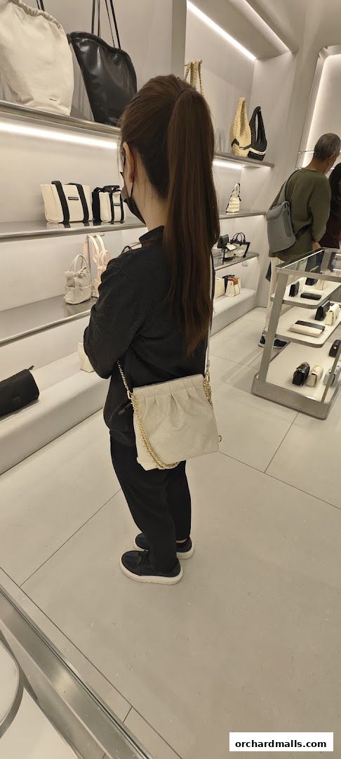 A woman tries on a quilted handbag in a modern retail store.
