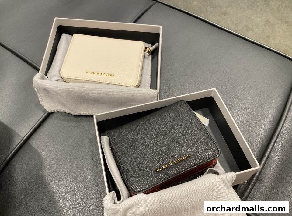 Two Charles & Keith wallets, one cream and one black, displayed in their boxes.