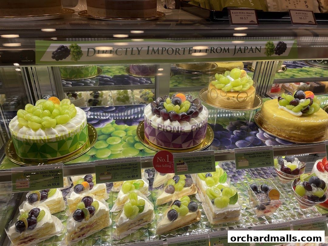 A display case filled with various cakes and desserts, many featuring fresh grapes.