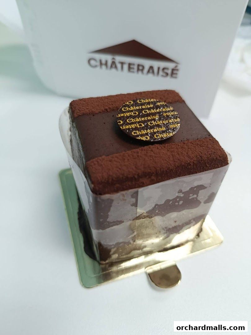 A rich chocolate cake with cocoa powder dusting and a branded circular topper.
