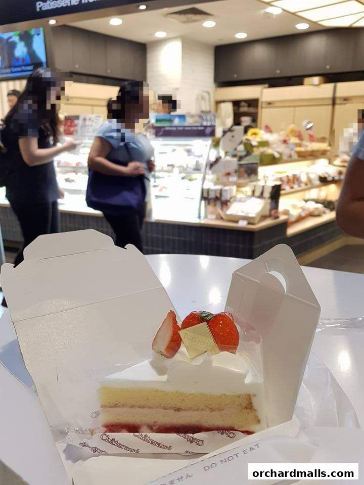 A slice of strawberry cake with whipped cream and fresh strawberries in a white box.