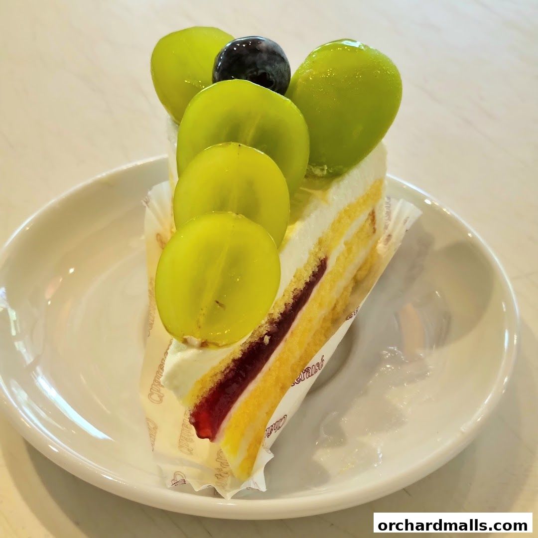 A slice of cake topped with fresh green grapes and a blueberry on a white plate.