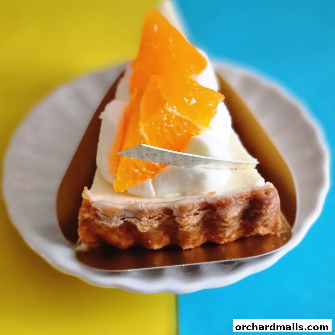 A slice of orange tart with whipped cream and fresh orange slices on a white plate.