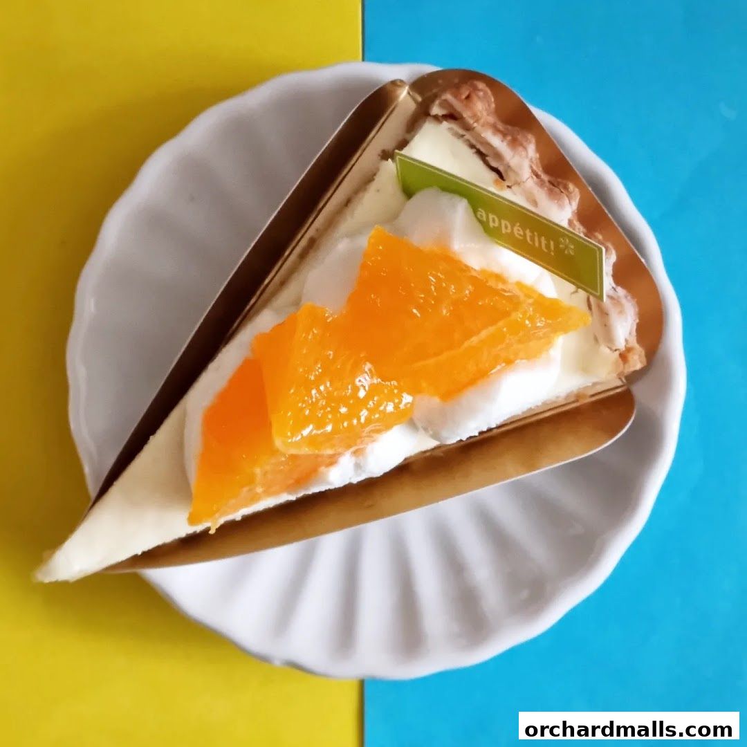 A slice of orange and cream cake on a white plate with a yellow and blue background.