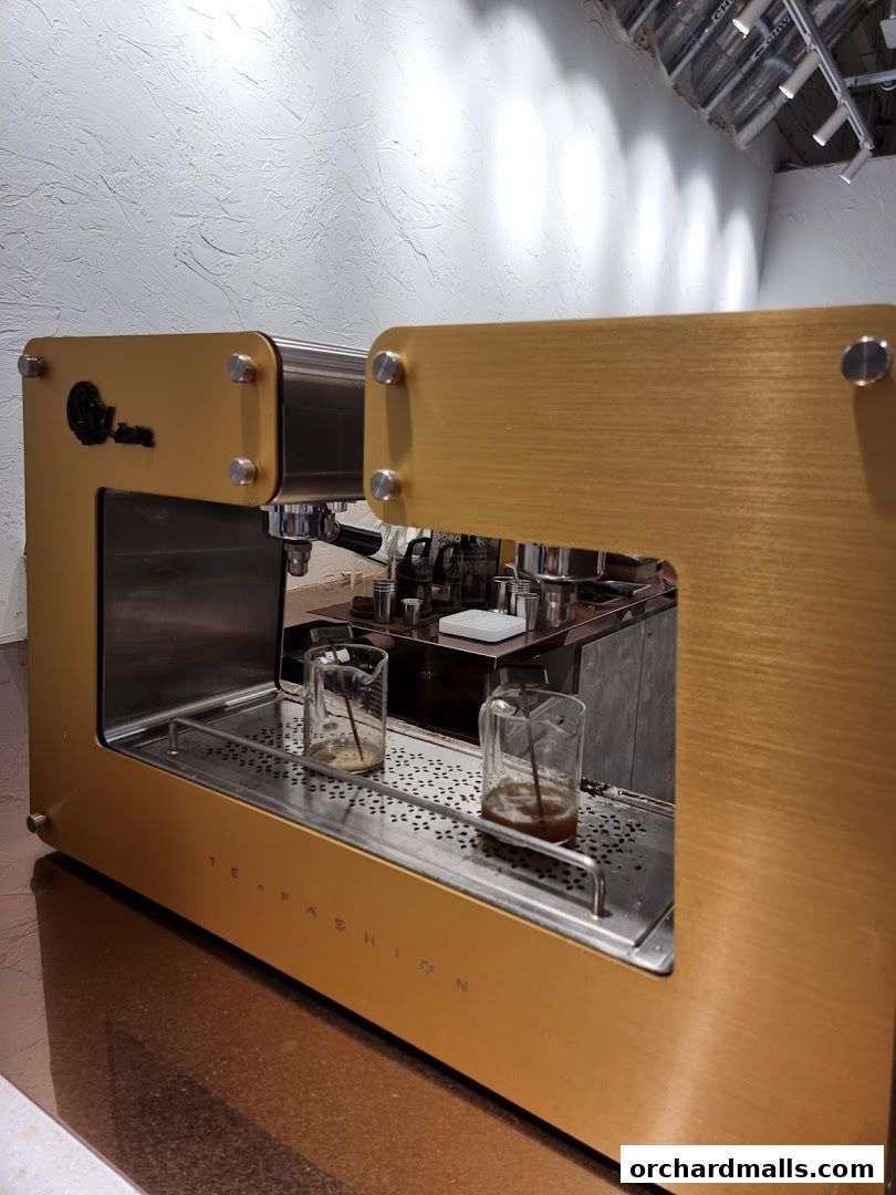 A close-up of a golden tea brewing machine with two beakers.