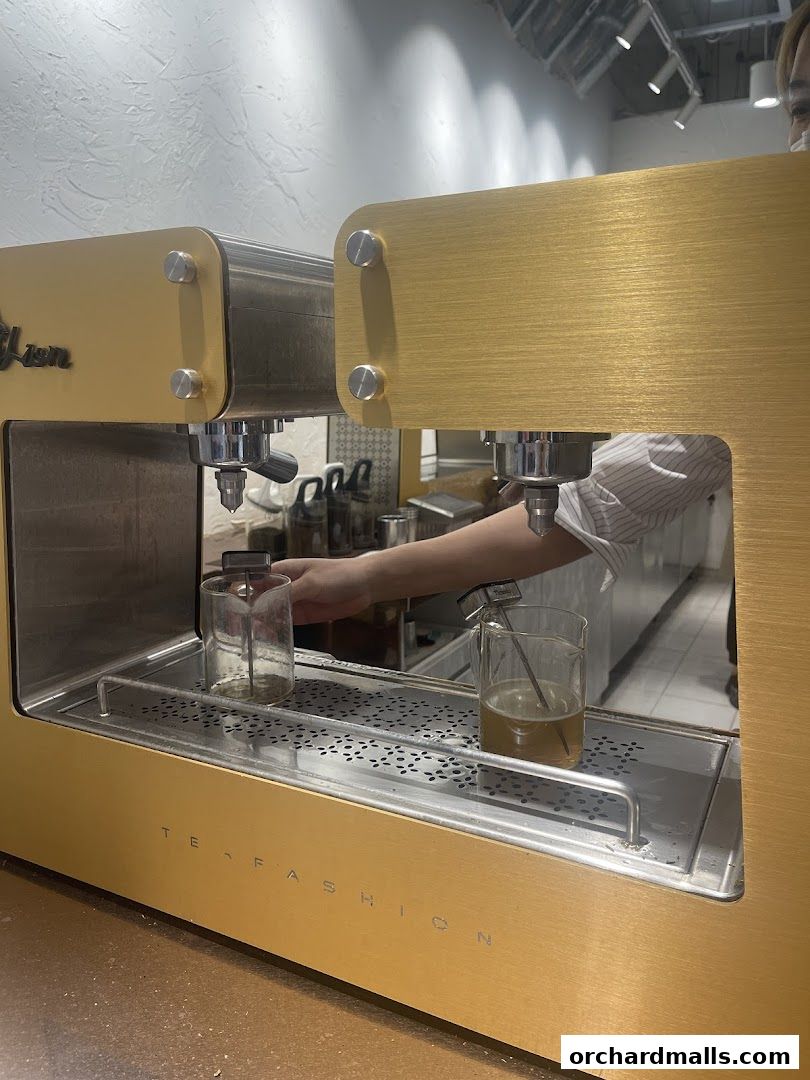 A close-up of a golden tea brewing machine with a hand preparing a drink.
