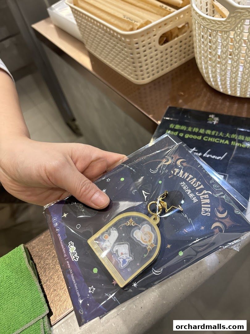 A hand holds a CHICHA San Chen fantasy series keychain and merchandise.