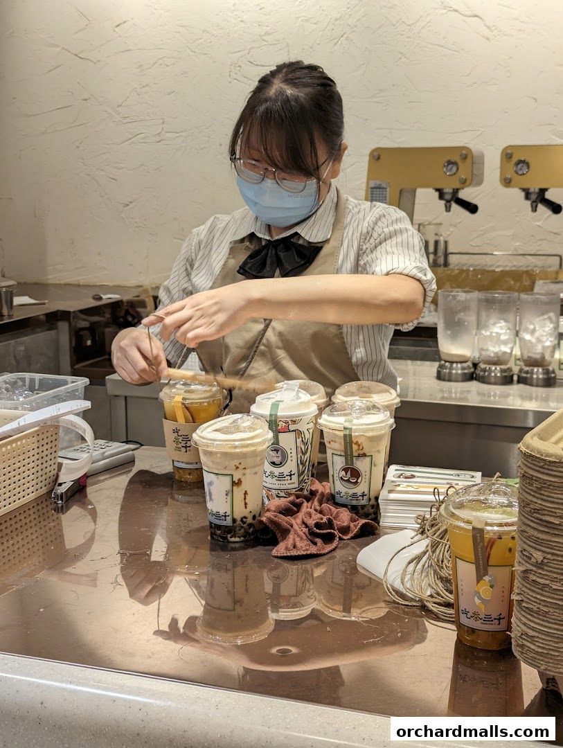 A staff member prepares drinks behind a counter with several bubble tea cups.