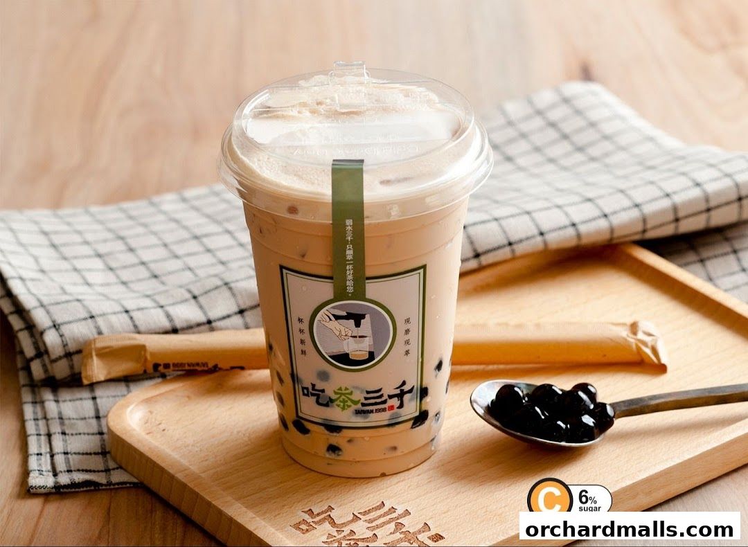 A cup of bubble tea with tapioca pearls on a wooden tray with a spoon.