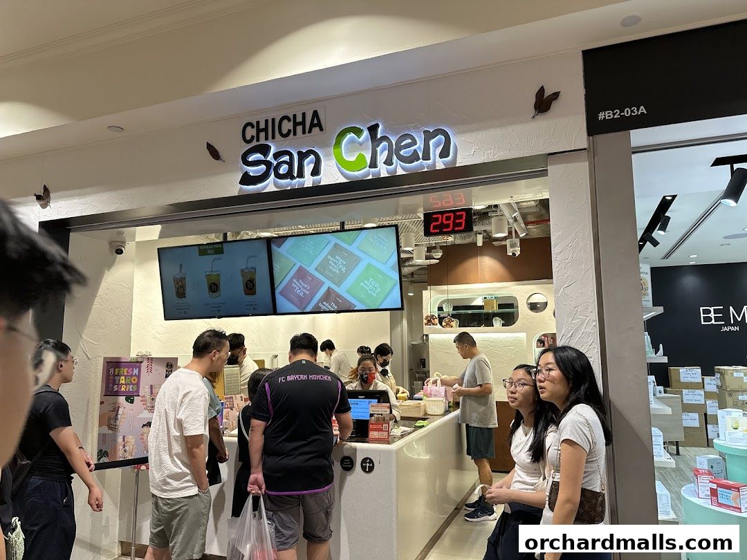 Customers queue at CHICHA San Chen, a bubble tea shop with digital displays and product advertisements.