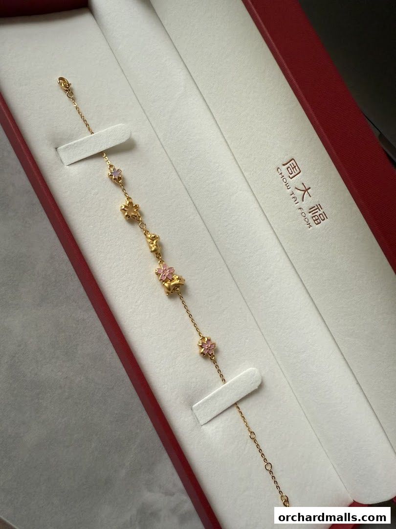 A delicate gold bracelet with floral charms presented in a red jewelry box.