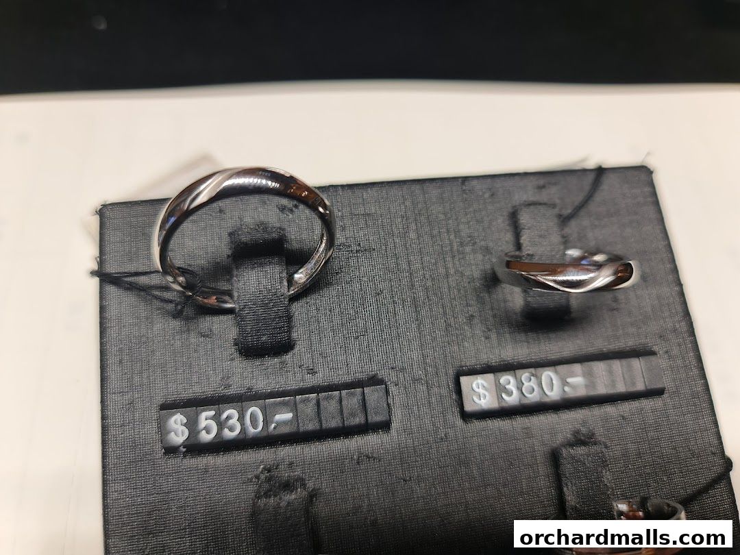 Close-up of two elegant silver rings displayed on black stands with price tags.