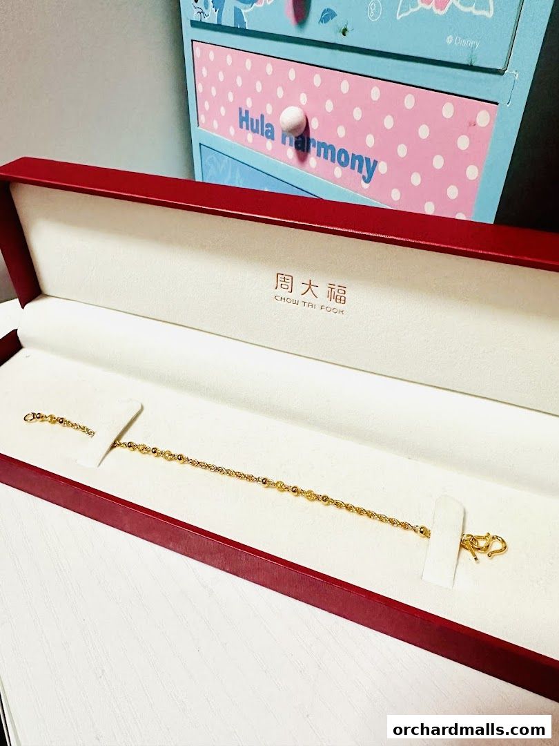 A gold bracelet displayed in a red jewelry box with the Chow Tai Fook logo.