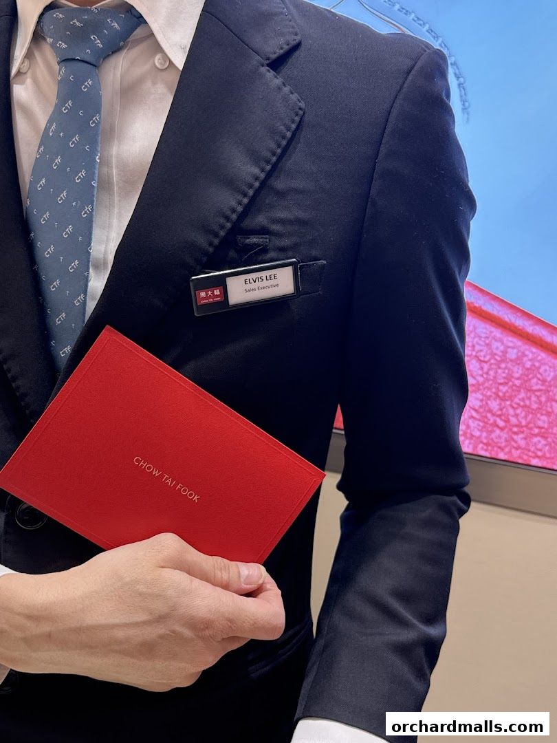 A person in a suit holding a red Chow Tai Fook booklet with a name tag.