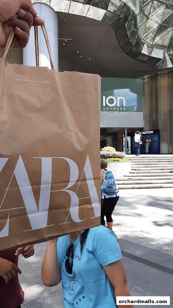 A person holds a Zara shopping bag in front of the ION Orchard building.