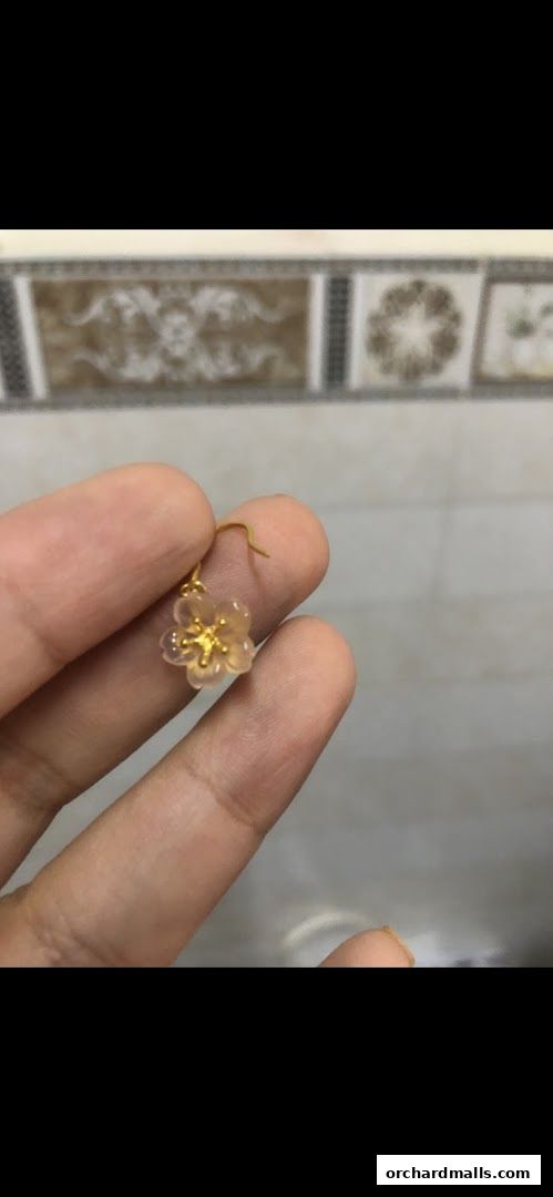 A hand holds a delicate gold earring with a translucent flower charm.